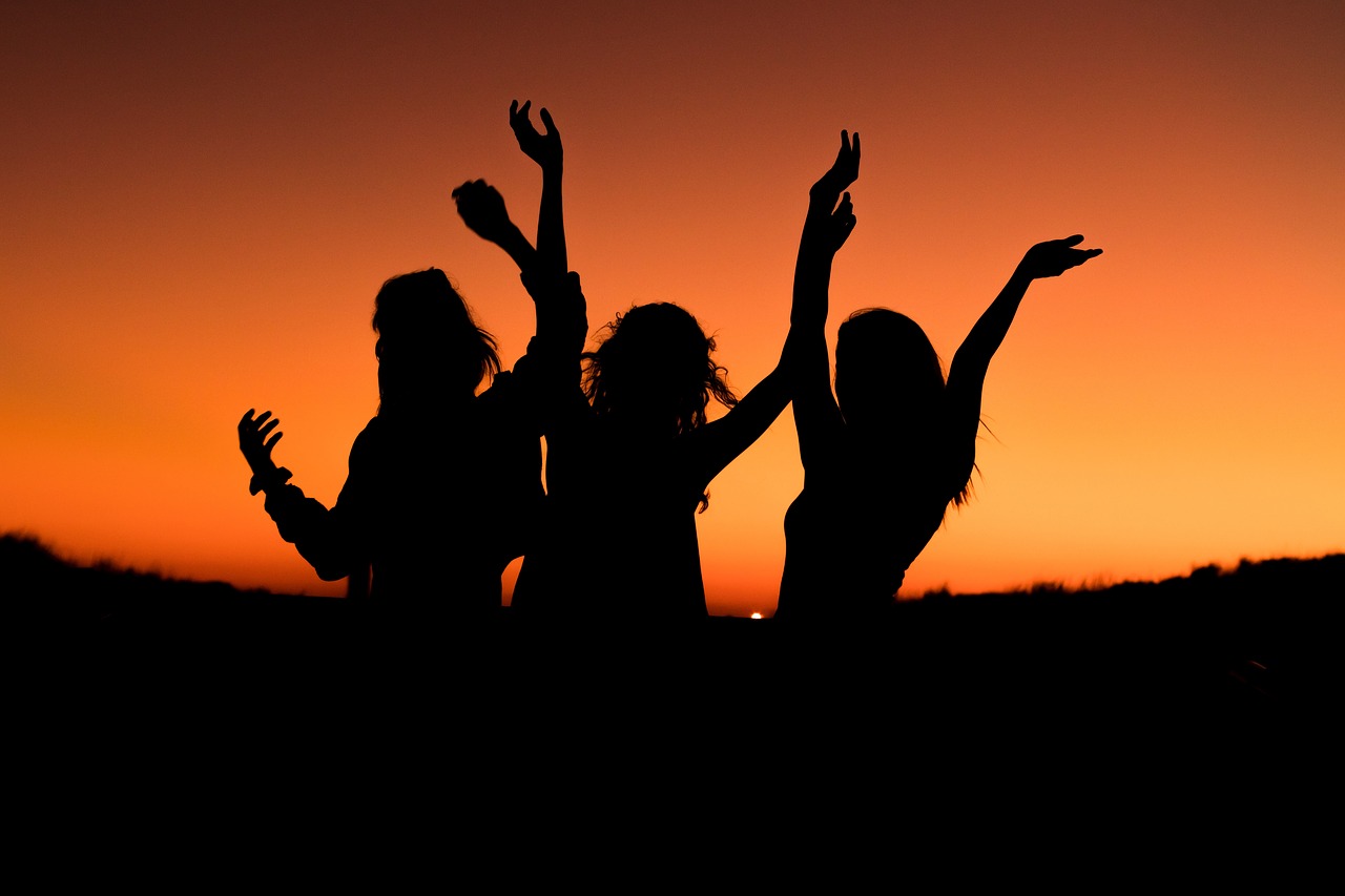 Three silhouettes of happy women set against a sunset.